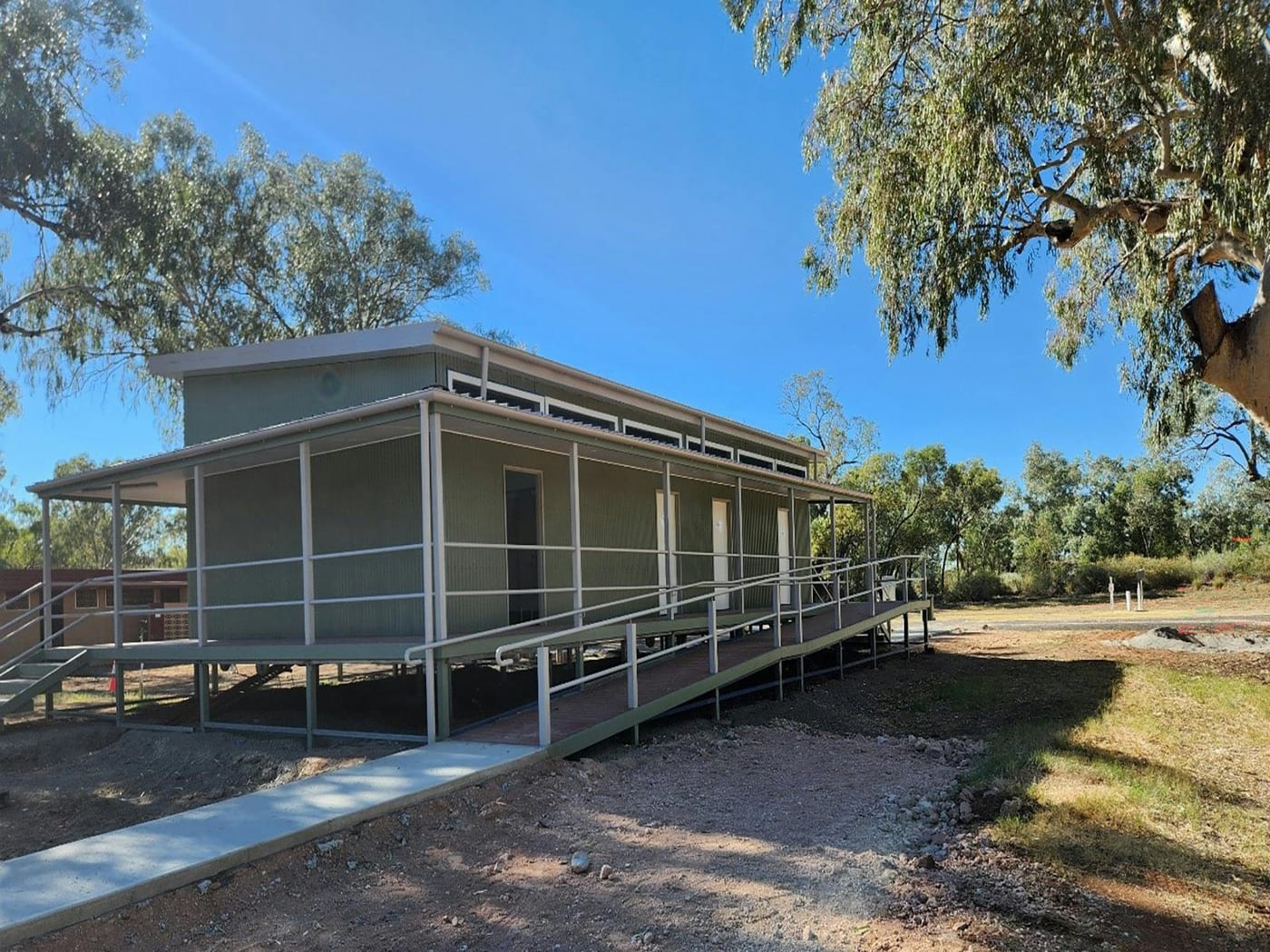 The new amenities block at Victory Caravan Park, Wilcannia: a raised demountable building with a wheelchair ramp, under river gums.
