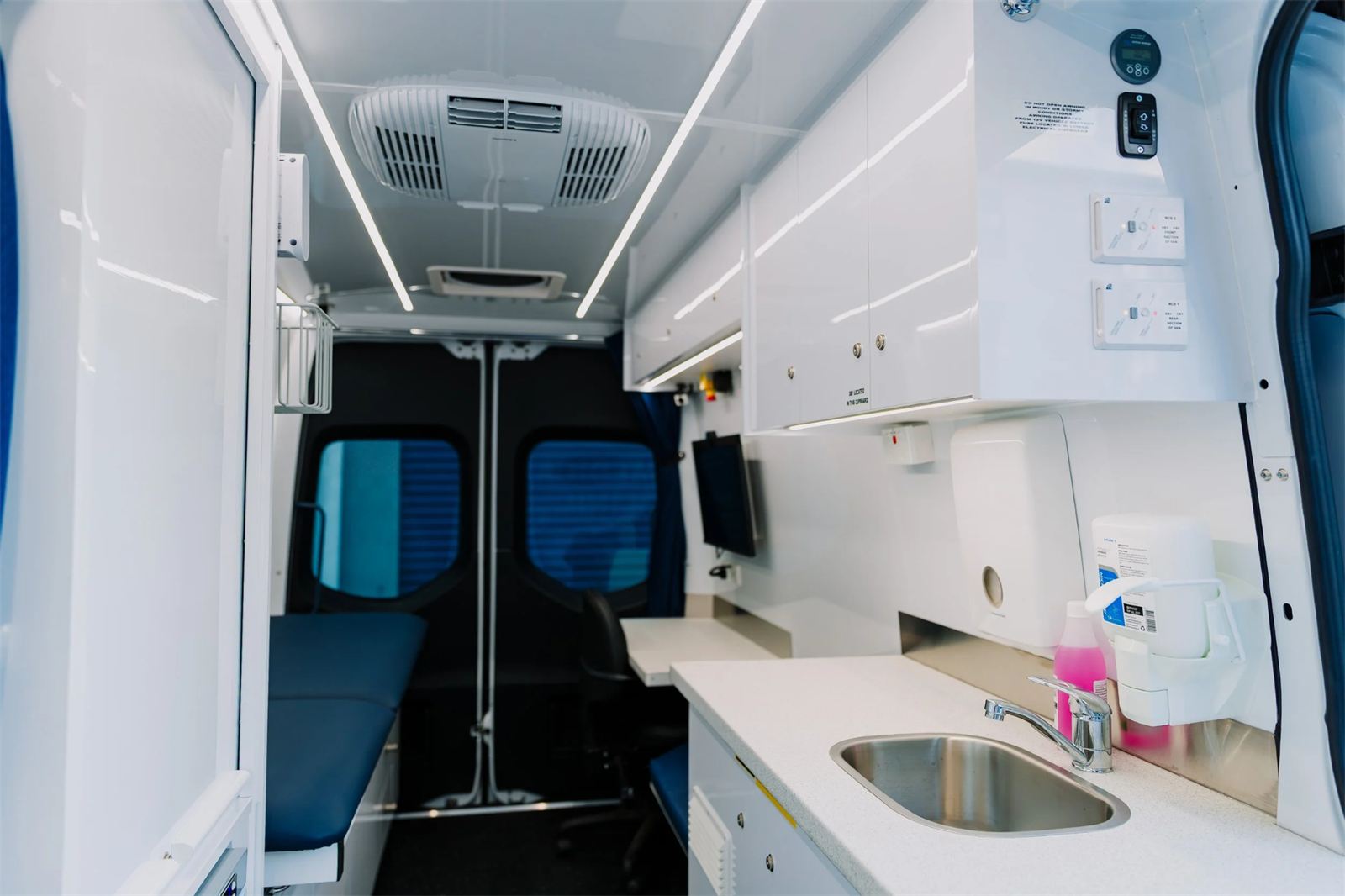 The mobile clinic interior, showing the consulting bench, examination bed, sink and telehealth screen.